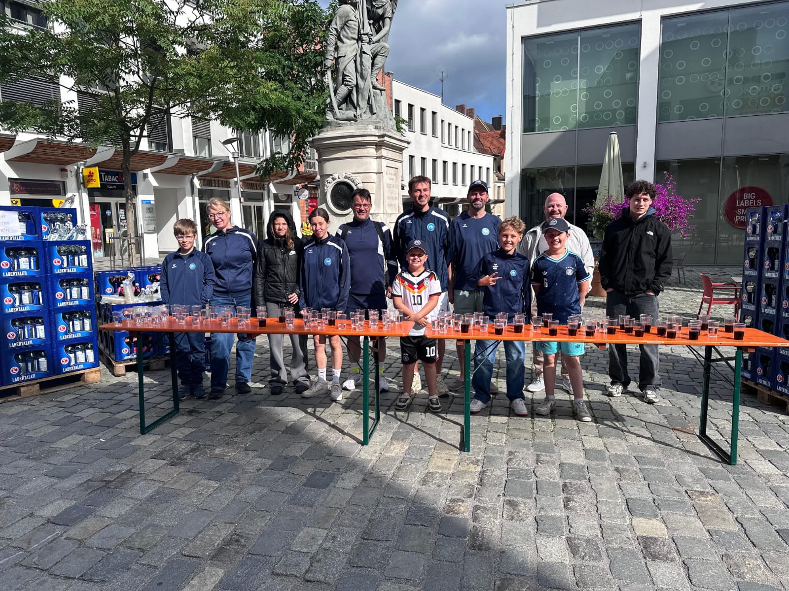 DJK Straubing Vereinsteam am Aktionsstand auf dem Theresienplatz Straubing, Juni 2026 – Erwachsene und Kinder in Vereinskleidung stehen hinter einem Tisch mit Gläsern.