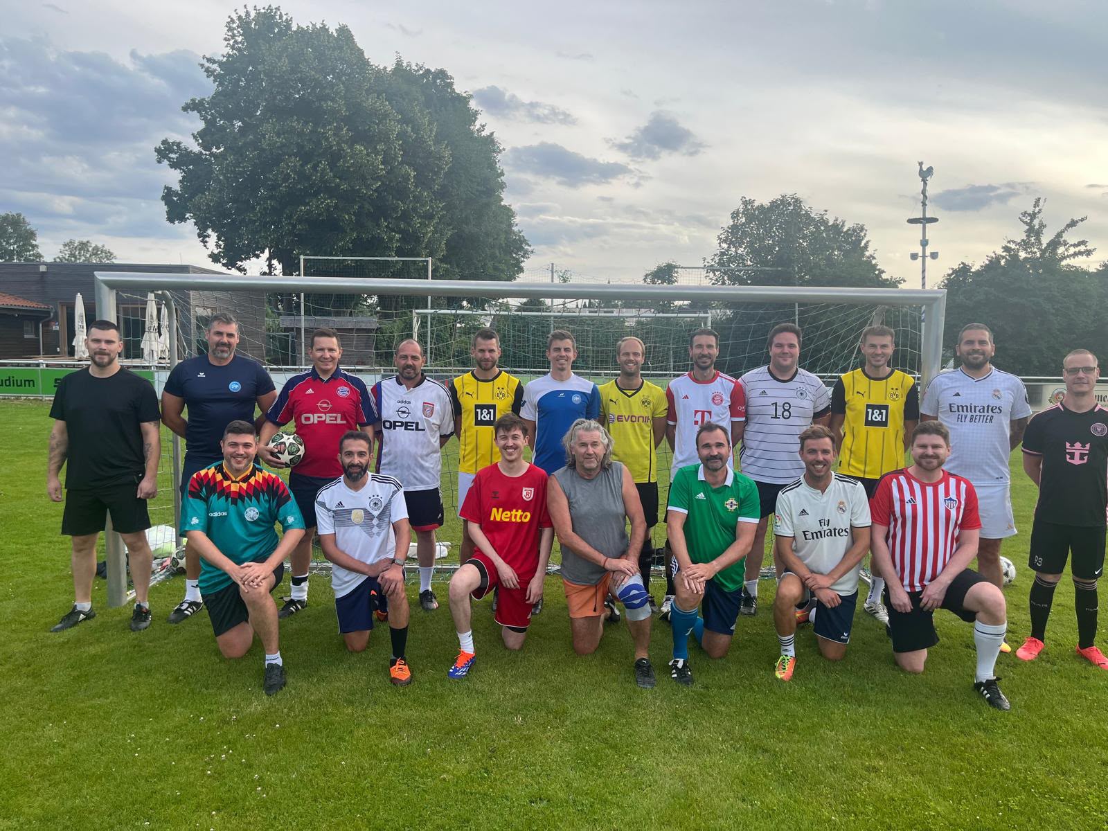 Gruppenfoto der Herren-Hobbymannschaft DJK SB Straubing im Trikot-Mix aus Bundesliga-, Nationaltrikots und Retro-Jerseys vor dem Fußballtor auf dem Sportgelände in Straubing
