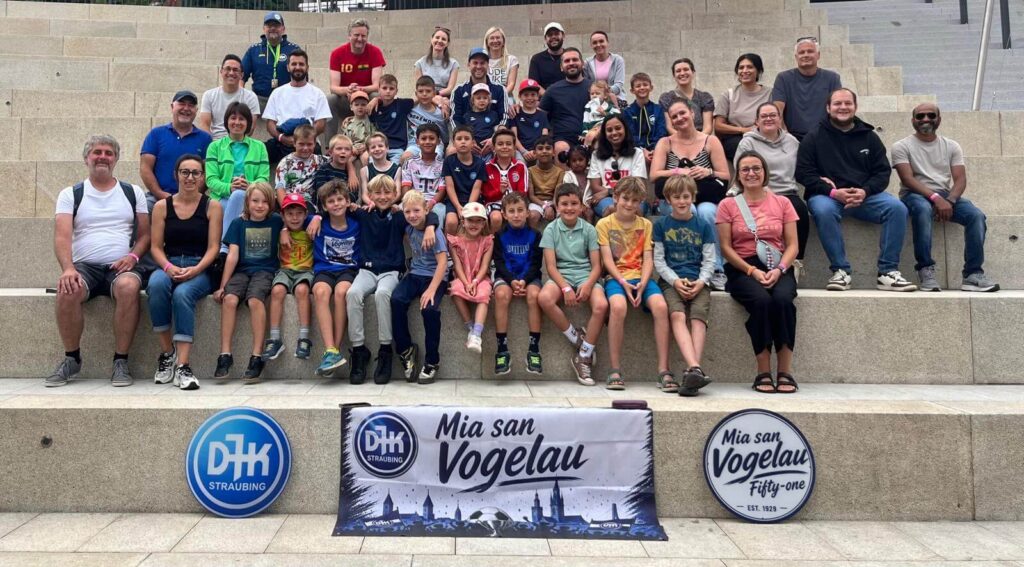 Gruppenfoto der E2/F-Jugend der DJK SB Straubing mit Trainern, Eltern und Geschwistern beim Mannschaftsausflug in den Edelwies Freizeitpark 2026 vor dem Mia-san-Vogelau-Banner.