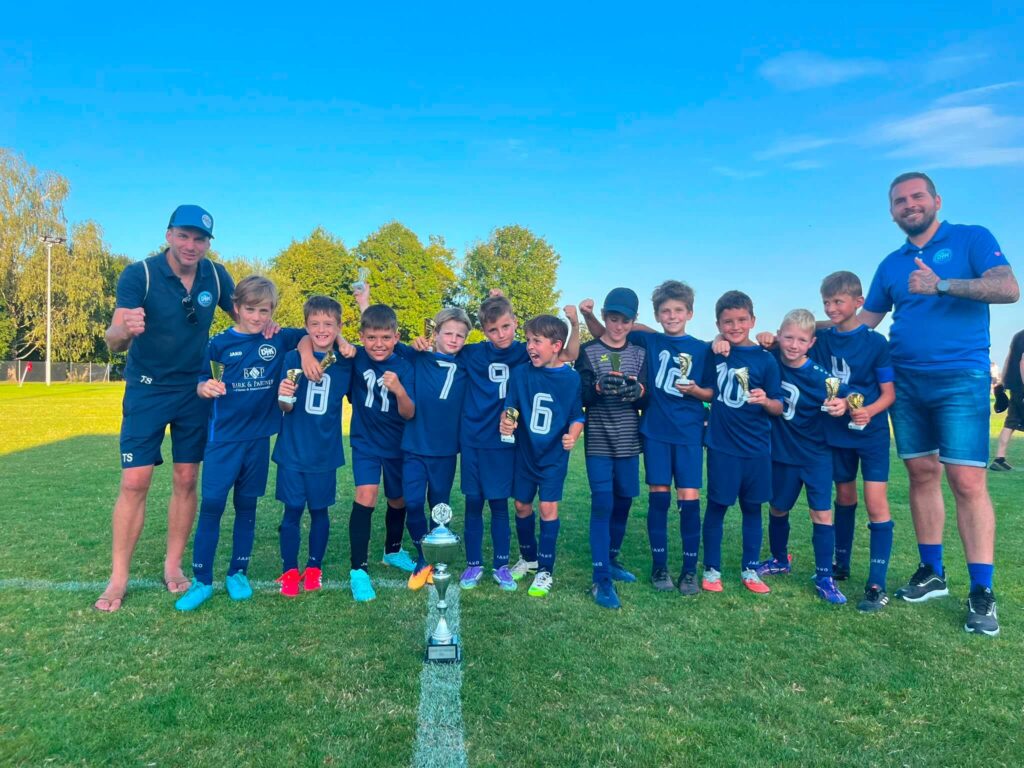 F1-Jugend der DJK SB Straubing mit Trainern Sinisa Stojanovic und Tom Straubinger nach dem Sieg beim Kiwanis Cup 2026 in Alburg mit Siegerpokal auf dem Spielfeld.