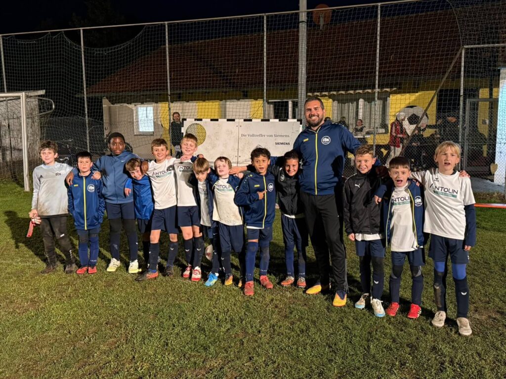 U11-Mannschaft (E-Jugend) der DJK SB Straubing mit Trainer jubelnd beim Teamfoto am Abend nach dem Spiel, Herbst 2026